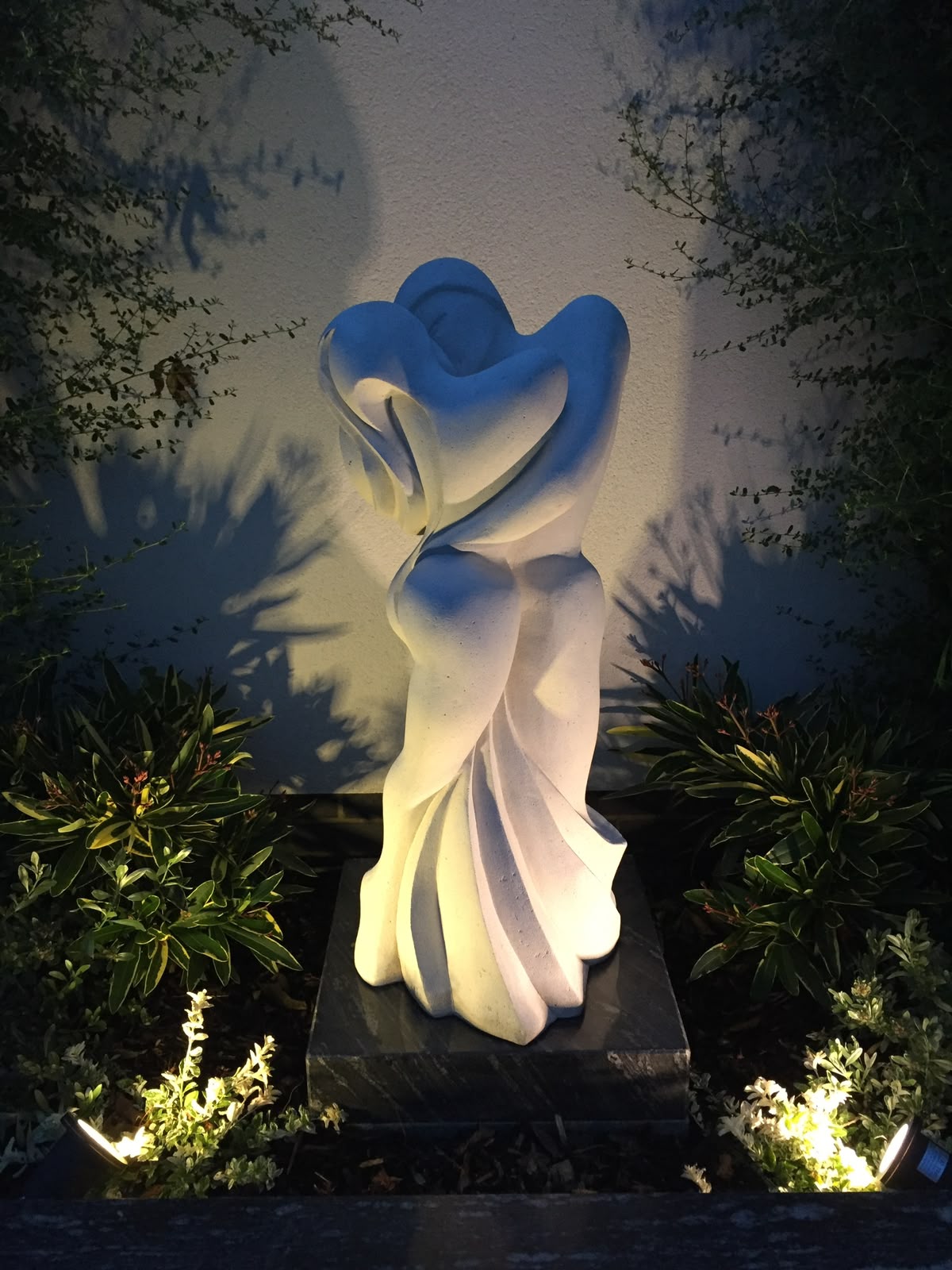 Where it started – illuminated stone sculpture Illuminated pale stone sculpture of an embracing seated figure in a garden