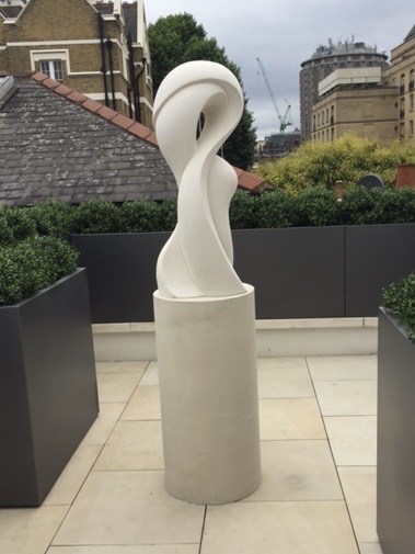 White abstract stone sculpture on a cylindrical plinth in a roof garden