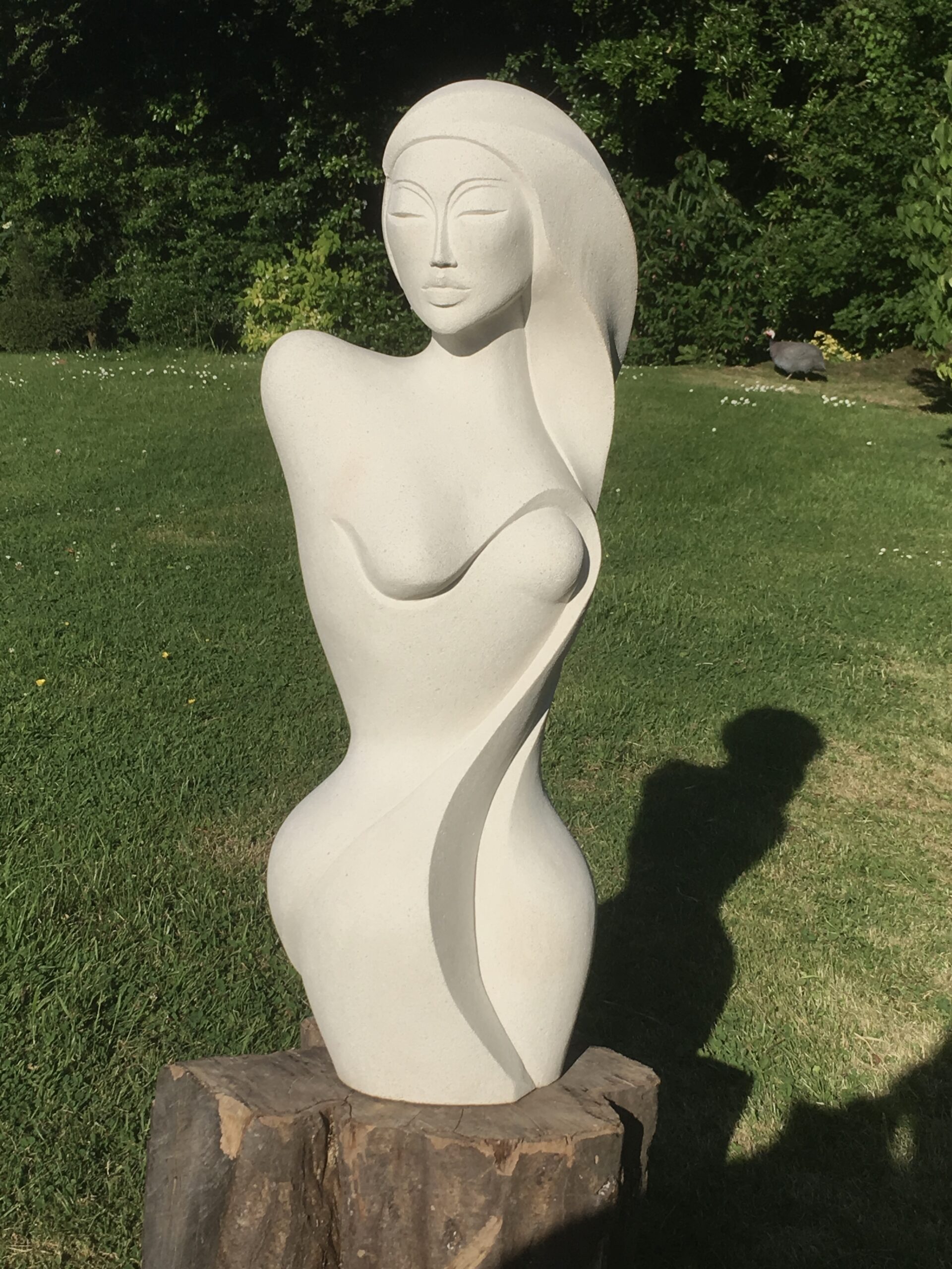 Pale figurative stone sculpture standing in a garden